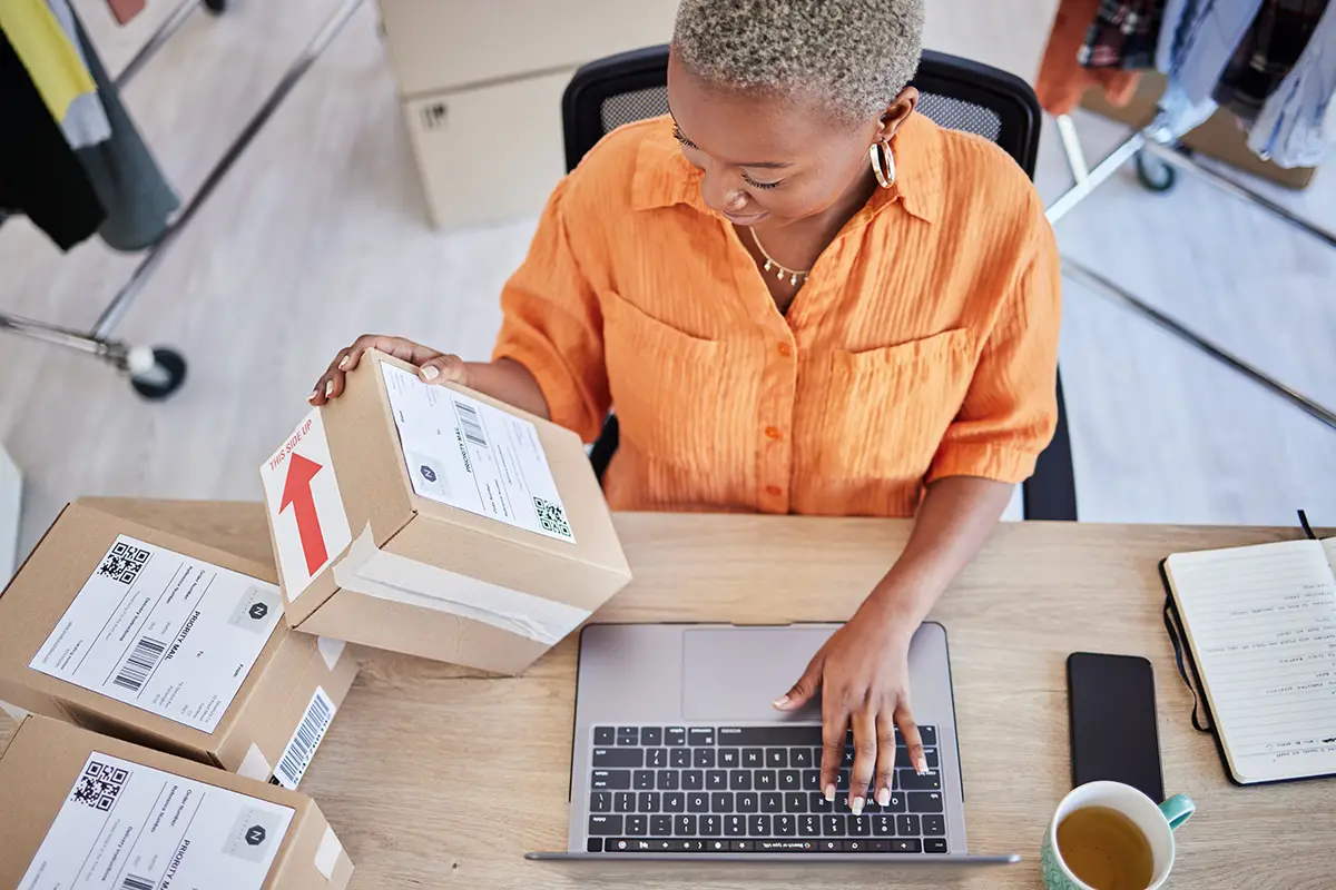 A female small business owner with parcels and a laptop computer using free multi-carrier shipping software to print discounted shipping labels