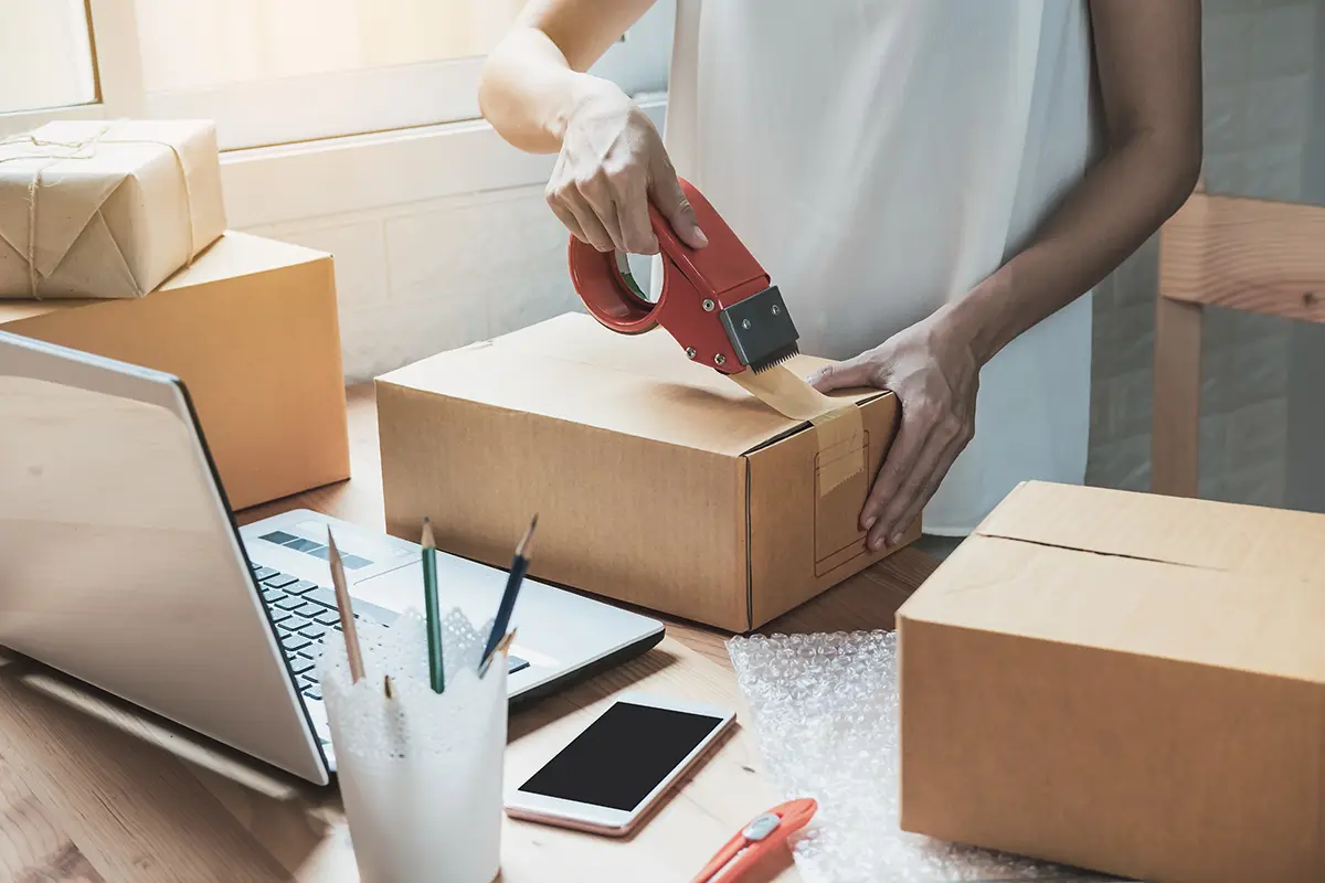 Small business owner with laptop and parcels taping a box to get started with international shipping